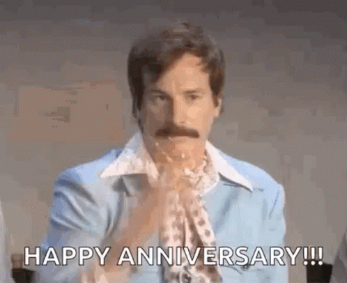 a man with a mustache is sitting at a table and saying `` happy anniversary ! ''